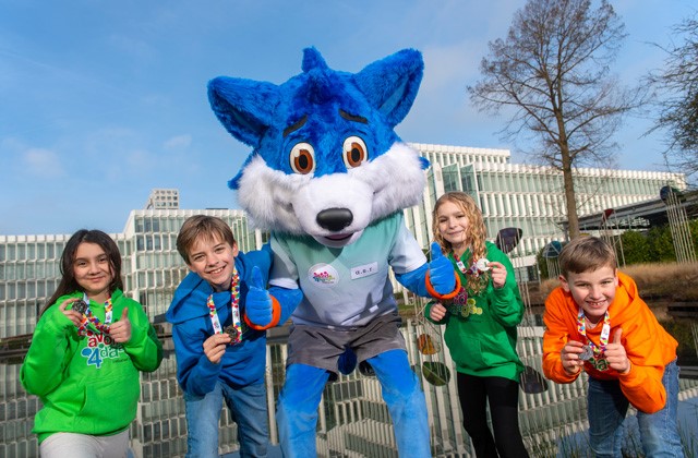 Vier kinderen tonen hun Avond4daagse medaille en steken hun duim omhoog, samen met Fiero